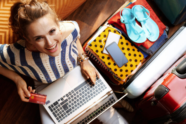 Uśmiechnięta młoda kobieta obok spakowanej walizki płacąca online za wakacje.
